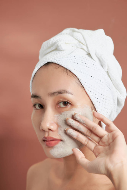 Spa Asian girl applying facial clay mask. Beauty treatments. Over blue background. - 写真・画像