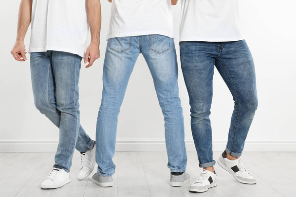 Group of young men in stylish jeans near white wall, closeup - Photo, Image