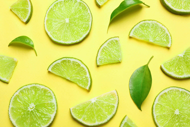 Juicy fresh lime slices and green leaves on yellow background, flat lay - Foto, Imagem