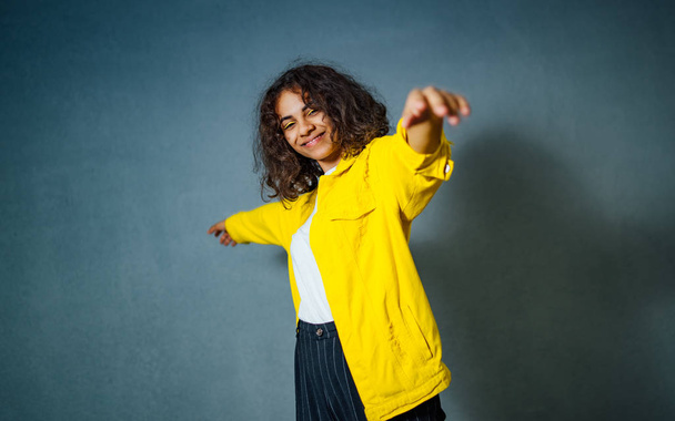 Young beautiful gorgeous female model in yellow jacket with curly hair posing against grey wall. Modern girl. Positive emotions concept. Closeup - Foto, Imagem