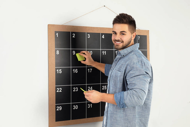 Young man putting sticky note on board calendar - Foto, Imagen