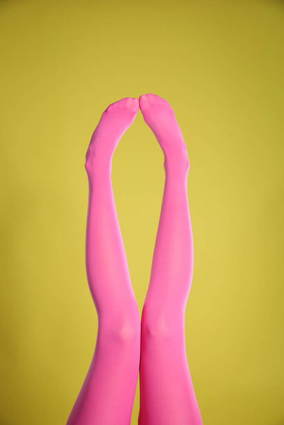Woman wearing pink tights on yellow background, closeup of legs - Foto, Imagem