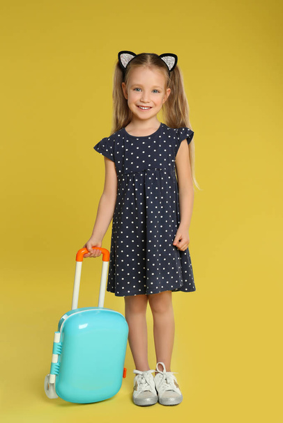 Cute little girl with suitcase on yellow background - Foto, immagini