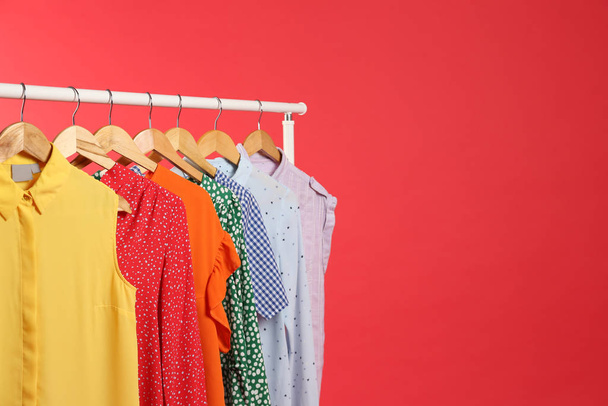 Bright clothes hanging on rack against red background, space for text. Rainbow colors - 写真・画像