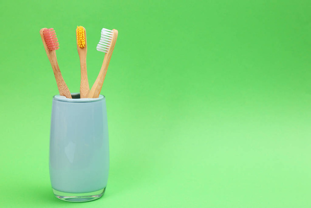 Bamboo toothbrushes in holder on green background, space for tex - 写真・画像