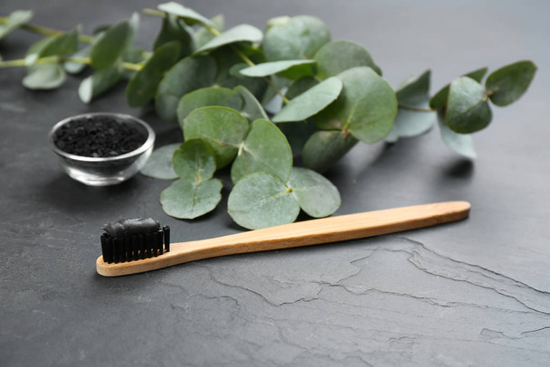 Bamboo toothbrush with charcoal paste on black stone table - Фото, изображение