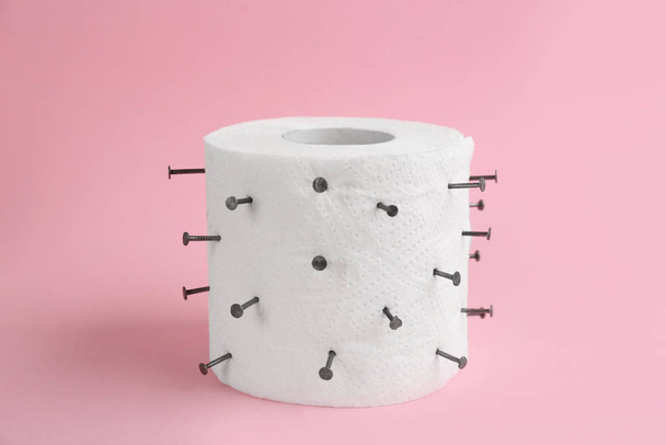 Roll of toilet paper with nails on pink. Hemorrhoid problems - Photo, Image