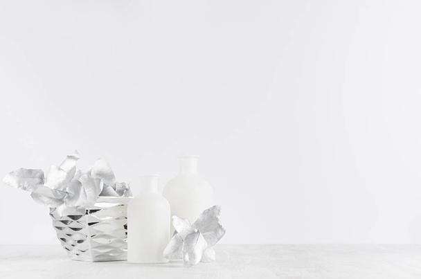 Decoraciones blancas contemporáneas simples para el interior: botellas de vidrio blanco, tazón de plata, hojas sobre fondo de madera blanca, espacio para copiar
. - Foto, Imagen