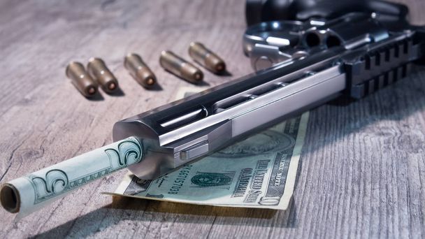 Пистолет с пулями и деньгами лежит на деревянном столе. Револьвер крупным планом
. - Фото, изображение
