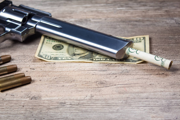 A pistol with bullets and money dollars lies on wooden the table. Revolver close-up. - Photo, Image