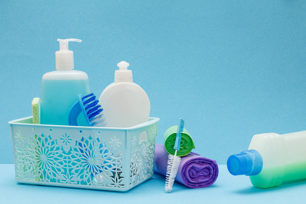 Flessen afwasmiddel in mand, sponzen en borstels op blauwe achtergrond. - Foto, afbeelding