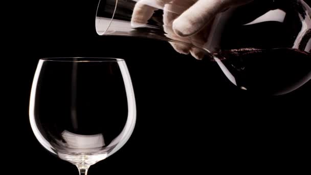 Egy üvegből készült vörösbor egy fekete hátterű pohárba ömlik. Közelről. Fekete mágia 6k kamera. - Felvétel, videó