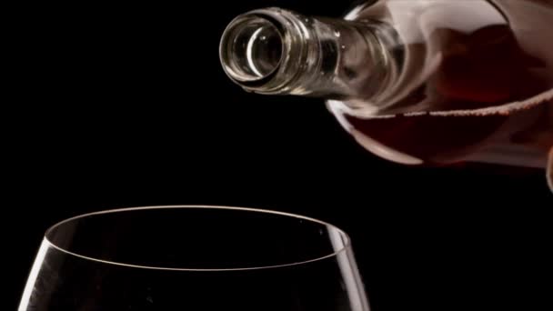 Rosafarbener Wein aus einer Flasche ergießt sich in ein Glas auf schwarzem Hintergrund. Nahaufnahme. Blackmagic 6k Kamera. - Filmmaterial, Video