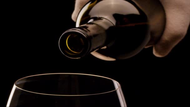 O vinho tinto de uma garrafa derrama em um copo em um fundo preto. Quase tiro. Blackmagic 6K câmera
. - Filmagem, Vídeo