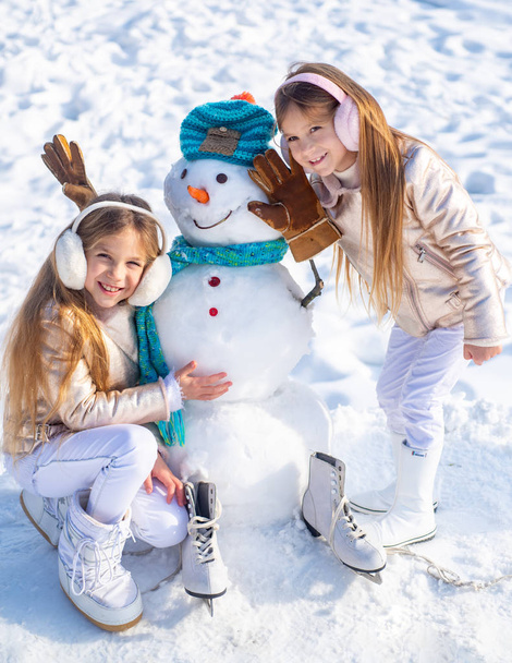 Счастливые дети играют со снеговиком на снежной зимней прогулке. Счастливое зимнее время для детей
. - Фото, изображение
