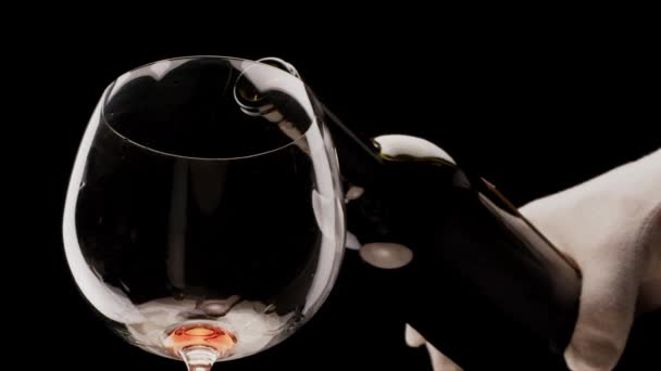 Rotwein aus einer Flasche ergießt sich in ein Glas auf schwarzem Hintergrund. Nahaufnahme. Blackmagic 6k Kamera. - Filmmaterial, Video