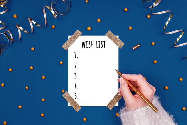 La mujer escribe la lista de deseos de Año Nuevo. Ilustración plana en oro y colores azules clásicos con tarjeta blanca aislada
 - Foto, imagen