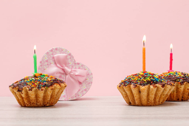 Muffins d'anniversaire avec bougie festive brûlante et boîte cadeau sur le fond rose
. - Photo, image