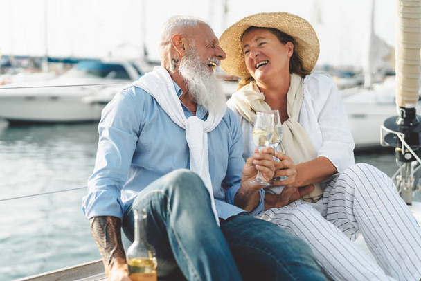 Senior couple toasting champagne on sailboat vacation - Happy elderly people having fun celebrating wedding anniversary on boat trip - Love relationship and travel lifestyle concept - Photo, Image