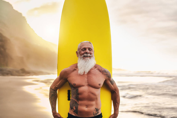 Щасливий підходить старший, розважається серфінгом під час заходу сонця Спортивний бородатий чоловік тренується з дошкою для серфінгу на пляжі Літні здорові люди стиль життя та концепція екстремального спорту
 - Фото, зображення
