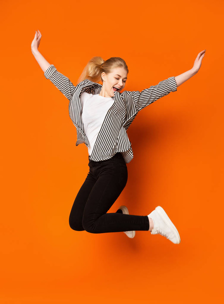Euphoric teen girl jumping over orange studio background - Foto, Bild