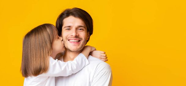 Маленькая девочка целует своего счастливого отца на жёлтом фоне
 - Фото, изображение