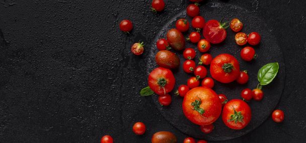 Kırmızı büyük ve küçük domatesler fesleğen yaprağıyla siyaha boyanmış. - Fotoğraf, Görsel