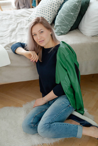 Blonde woman is sitting near the cozy bed - Фото, изображение