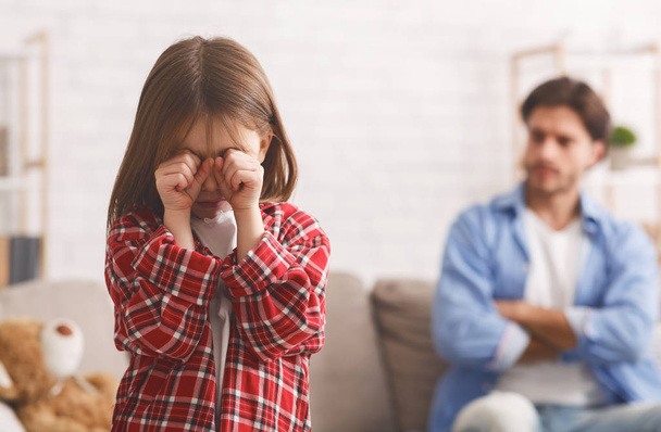 Little girl crying after quarrel wIth father, angry dad behind - Foto, imagen