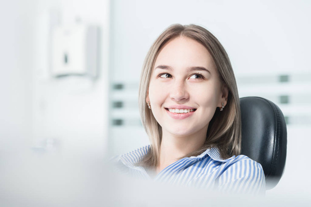 Portret van een aantrekkelijk glimlachend meisje blonde in een tandheelkundige stoel. Gelukkige klant tandheelkundige kabinet - Foto, afbeelding