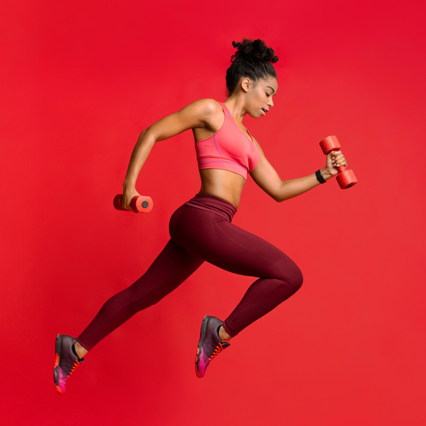 Active african woman training wth dumbbells over red background - Foto, imagen