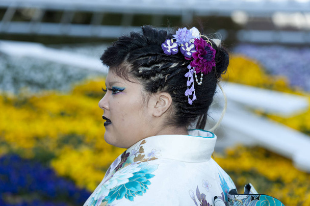 Hermosa adolescente japonesa que usa kimono tradicional mirando de lado con un primer plano en el ornamento para el cabello que celebra el Día de la Venida de la Edad en la ciudad de Fuji, Japón. Fondo con flores amarillas desenfocadas
. - Foto, imagen