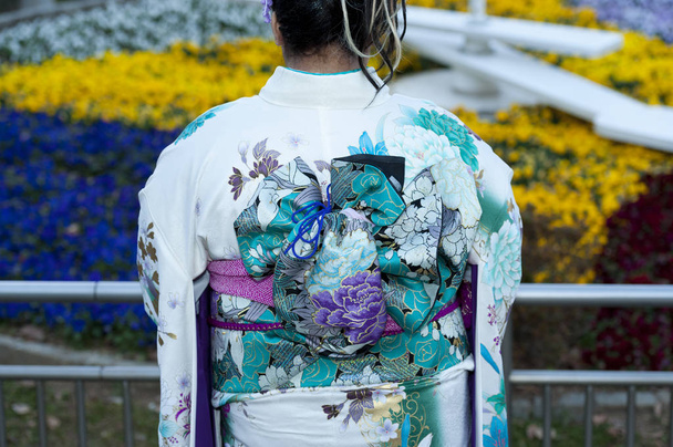 Прекрасний японський підліток, одягнений у традиційне кімоно, відзначає День пришестя в місті Фудзі (Японія). Тло з розфарбованими барвистими квітами.. - Фото, зображення