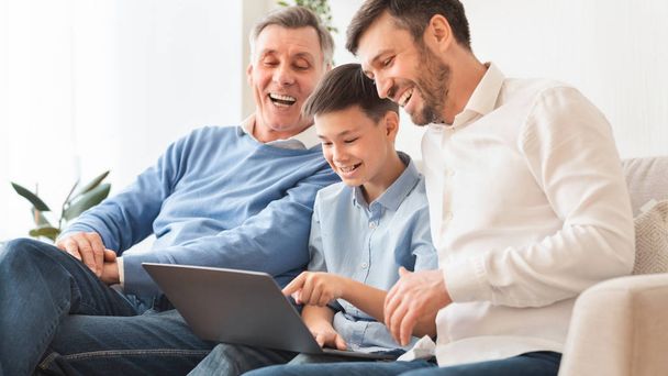 Хлопчик використовує ноутбук сидить між батьком і дідусем вдома
 - Фото, зображення