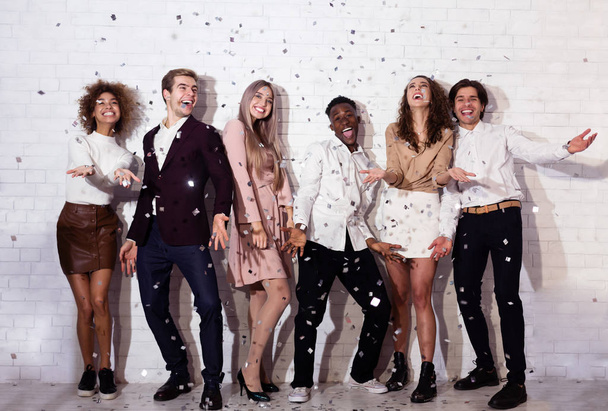 Pozitív fiatalok állnak alatt Falling Confetti szórakozás beltéri - Fotó, kép