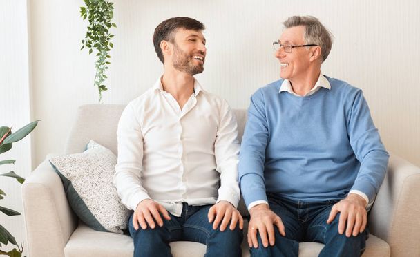 Älterer Vater und älterer Sohn lächelnd auf Couch zu Hause - Foto, Bild