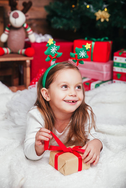 Happy little smiling girl with christmas gift box lying near Christmas tree - Foto, immagini