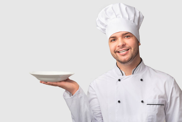 Σεφ άνθρωπος κρατώντας άδειο πιάτο χαμογελώντας στέκεται πάνω από το λευκό φόντο - Φωτογραφία, εικόνα