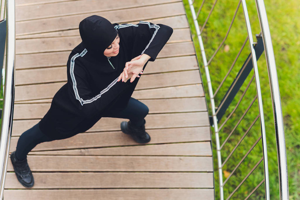 Chica Hijab haciendo ejercicio en el puente de la pasarela temprano en la mañana. Mujer musulmana usando ropa deportiva haciendo ejercicio de estiramiento al aire libre
. - Foto, imagen