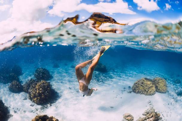 Gratis duiker jong meisje met gele vinnen glijdt over zandige bodem  - Foto, afbeelding