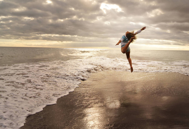 Gymnast in jump in ocean weaves. - 写真・画像
