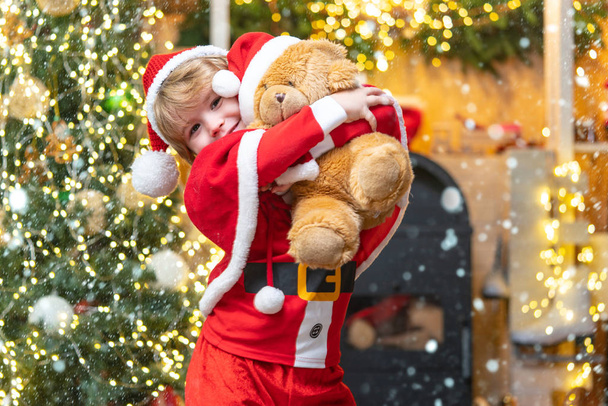 Dreamy toddler on Christmas eve. Christmas child. For Christmas and New Year posters. Delivery christmas gifts. Santa Claus kid boy with a teddy bear. Child in snow. - Zdjęcie, obraz