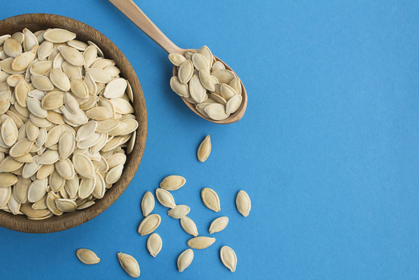 Pumpkin seeds in the brown bowl  and spoon on the blue  background. Copy space. Top view. - Foto, Bild