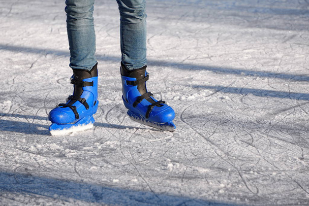 Patines de plástico azul brillante en el fondo de hielo rayado en un día soleado. entretenimiento en la temporada de invierno, deportes activos. piernas de un hombre en patines azules monta en una pista de hielo
. - Foto, Imagen