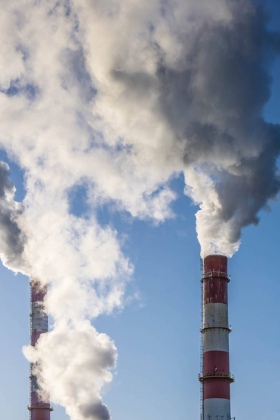 Industrial smokestacks with thick smoke clouds over blue sky. Global warming. Air pollution. - Photo, Image