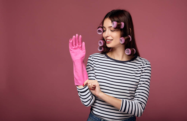 A young lady in curlers puts on gloves for cleaning. - Foto, Imagen