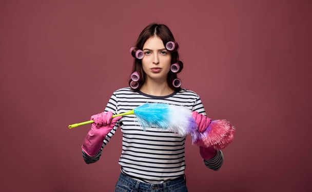 A serious lady in curlers holds a dust brush in her hands. - 写真・画像