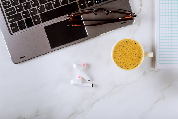 Irodai munkaasztal felülnézet laptoppal, jegyzettömbbel, poharakkal és kávéval, vezeték nélküli fülhallgatóval, szemüveggel - Fotó, kép