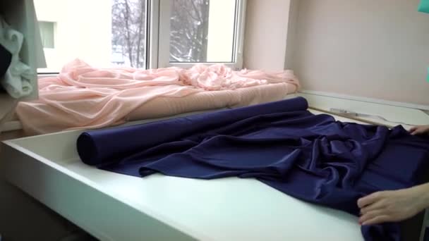 Young female spreading roll of blue satin fabric on table in fashion atelier - Video