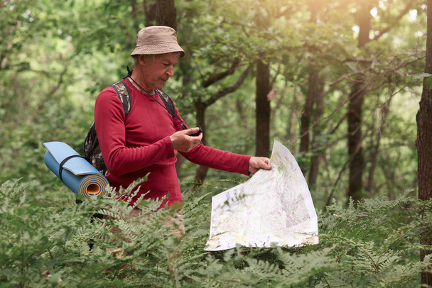 Coordination and navigation in the forest. Image of man holding compass and paper map in his hands, finding right way in wood, being lost while walking on path and enjoying beautiful nature. - Zdjęcie, obraz